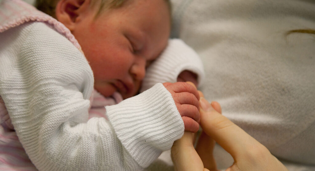 Schlafendes Baby hält sich am Finger fest